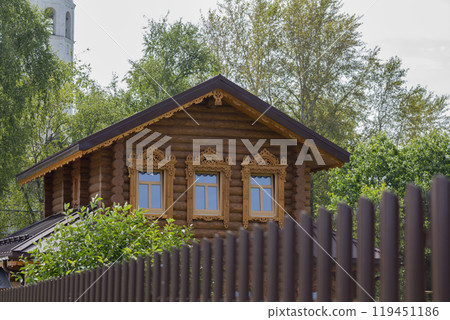 There is a timber cottage behind the fence. A wooden house behind a brick wall n summer 119451186