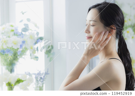A woman in a black camisole dress standing by the window 119452919
