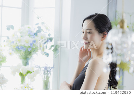 A woman in a black camisole dress standing by the window 119452920