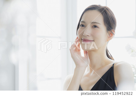 A woman in a black camisole dress standing by the window 119452922
