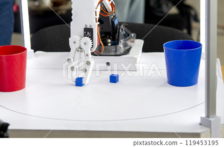 Robot automatic hand taking cubes and putting in glass. Automatic robotic arm distinguishing color of cube and putting in glass of same color. Automation, modern technologies. Artificial Intelligent Robot automatic hand taking cubes and putting in glass. Automatic robotic arm distinguishing color of cube and putting in glass of same color. Automation, modern technologies. Artificial Intelligent 119453195
