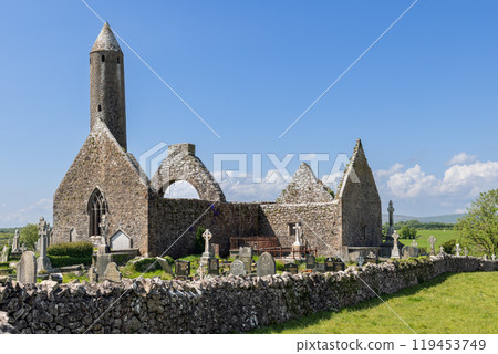 Kilmacduagh Abbey in County Galway, Ireland, features a round tower and medieval stone ruins surrounded by a historic cemetery Kilmacduagh Abbey in County Galway, Ireland, features a round tower and medieval stone ruins surrounded by a historic cemetery 119453749