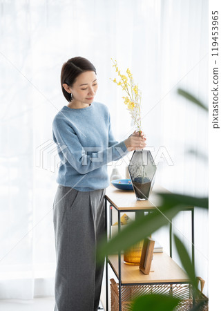 Woman arranging flowers in living room 119453965
