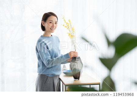Woman arranging flowers in living room 119453968