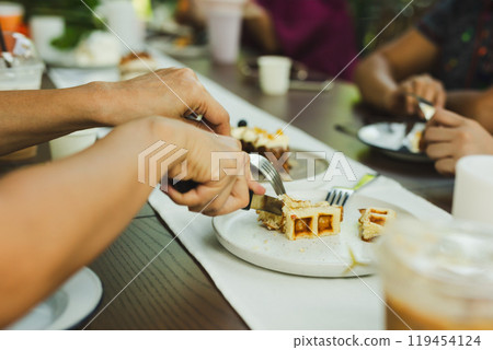 Woman hands cutting waffles with fork and knife on plate in cafe. Woman hands cutting waffles with fork and knife on plate in cafe. 119454124