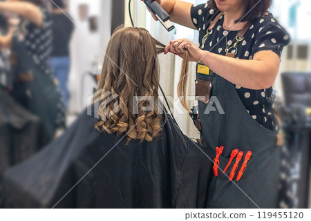 Hands of a hairdresser with a curling iron doing a girl's hair in a professional beauty salon Hands of a hairdresser with a curling iron doing a girl's hair in a professional beauty salon 119455120