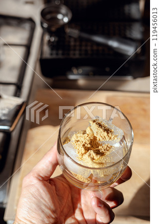 A glass filled with ice cubes and powdered Amanita muscaria mushroom on its surface, held in the hand, illuminated by natural sunlight. Preparing a homemade fly agaric elixir A glass filled with ice cubes and powdered Amanita muscaria mushroom on its surface, held in the hand, illuminated by natural sunlight. Preparing a homemade fly agaric elixir 119456013