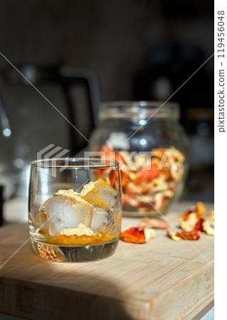 Preparation of fly agaric drink, ground powdered dry mushroom on ice cubes in a glass, illuminated by natural sunlight.  Homemade fly agaric elixir.   119456048