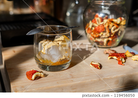Preparation of fly agaric drink, ground powdered dry mushroom on ice cubes in a glass, illuminated by natural sunlight. Homemade fly agaric elixir. Preparation of fly agaric drink, ground powdered dry mushroom on ice cubes in a glass, illuminated by natural sunlight. Homemade fly agaric elixir. 119456050