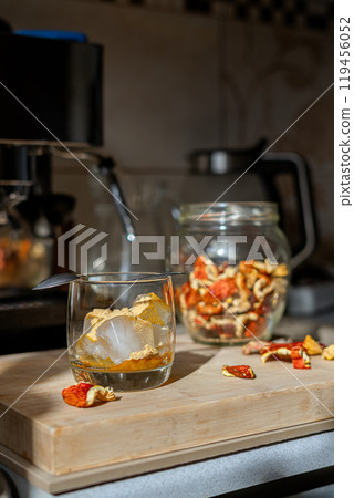 Preparation of fly agaric drink, ground powdered dry mushroom on ice cubes in a glass, illuminated by natural sunlight.  Homemade fly agaric elixir.   119456052
