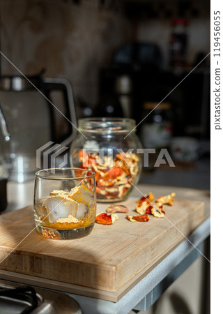 Preparation of fly agaric drink, ground powdered dry mushroom on ice cubes in a glass, illuminated by natural sunlight.  Homemade fly agaric elixir.   119456055