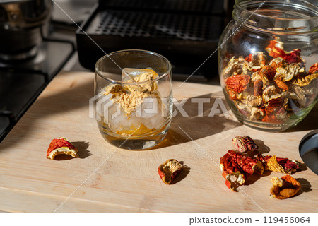 Preparation of fly agaric drink, ground powdered dry mushroom on ice cubes in a glass, illuminated by natural sunlight.  Homemade fly agaric elixir. Top View 119456064