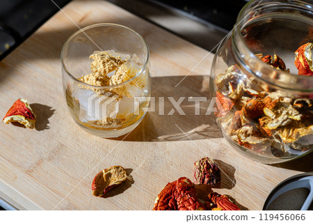 Preparation of fly agaric drink, ground powdered dry mushroom on ice cubes in a glass, illuminated by natural sunlight. Homemade fly agaric elixir. Top View Preparation of fly agaric drink, ground powdered dry mushroom on ice cubes in a glass, illuminated by natural sunlight. Homemade fly agaric elixir. Top View 119456066