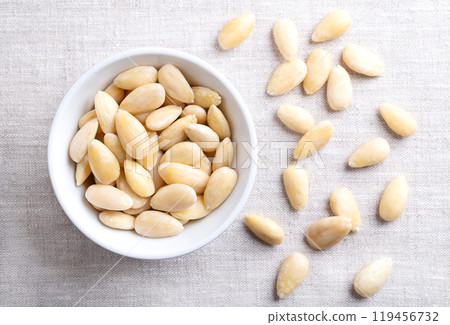 Freshly blanched almonds in a white bowl on linen. Shelled almonds that have been treated with hot water to soften the seed coat, which is then removed to reveal the seed. Fruits of Prunus amygdalus. Freshly blanched almonds in a white bowl on linen. Shelled almonds that have been treated with hot water to soften the seed coat, which is then removed to reveal the seed. Fruits of Prunus amygdalus. 119456732