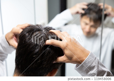 Middle-aged man doing scalp massage in front of bathroom mirror 119458006