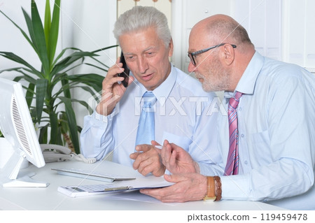 Two old business men sitting at desk and working Two old business men sitting at desk and working 119459478