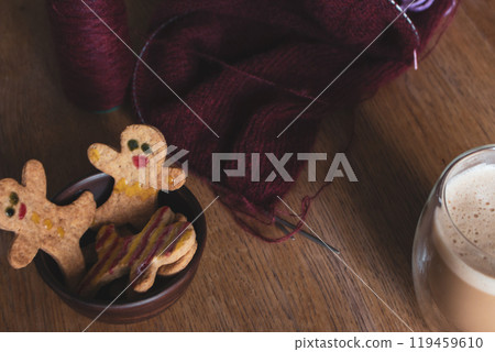 Gingerbread man cookies and red knitting with needles. Decorated cookie with smile and eyes and bobbin of wool yarn. Christmas cookies background. Homemade biscuits. Cinnamon cookies and red sweater Gingerbread man cookies and red knitting with needles. Decorated cookie with smile and eyes and bobbin of wool yarn. Christmas cookies background. Homemade biscuits. Cinnamon cookies and red sweater 119459610