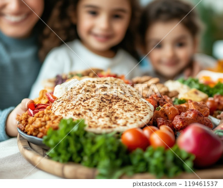 A vibrant platter of assorted dishes, featuring fresh vegetables and bread, enjoyed by smiling children in a cozy setting. 119461537