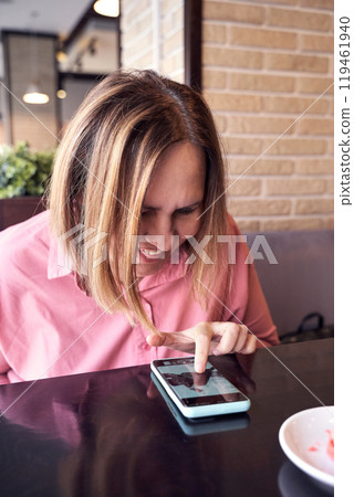 Woman in pink shirt smiling and using smartphone at cafe table with brick wall 119461940
