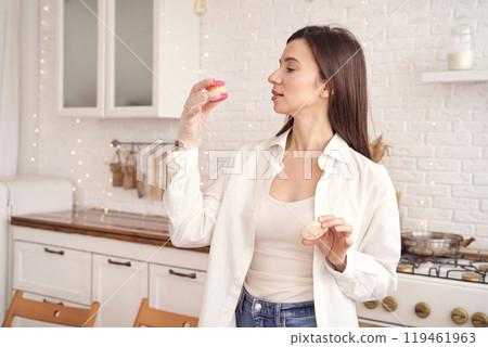 Woman enjoying macarons in modern kitchen setting with soft ambient lighting 119461963