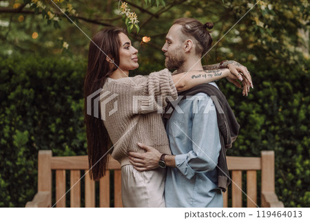 Happy loving couple enjoying their time together in park. Loving couple spending time together. Girl with tattoos. Tattooed woman. Beautiful fashionable couple of lovers on the street. 119464013