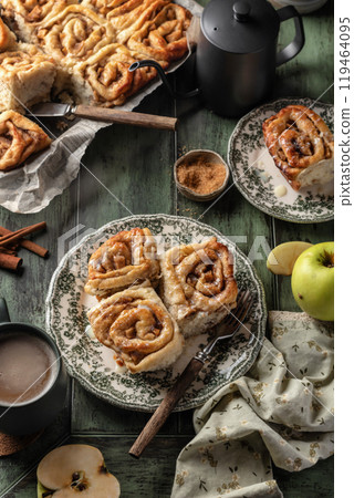 Autumn apple cinnamon rolls with frosting on green wooden background. Seasonal autumn homemade pastry cinnabons for breakfast 119464095