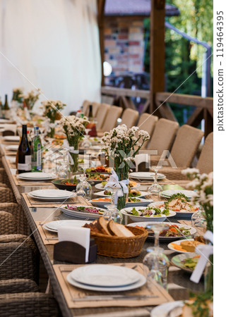 Elegant Outdoor Banquet Setup with Floral Decor and Gourmet Dishes in a Rustic Setting 119464395