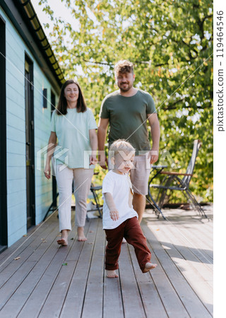 A joyful family walking together on a sunny day, with their child leading the way in playful moment 119464546