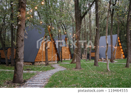 Modern A-frame cabins with glowing string lights in forest environment, ideal for a peaceful retreat Modern A-frame cabins with glowing string lights in forest environment, ideal for a peaceful retreat 119464555