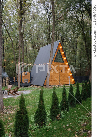 A-frame cabin in the forest with warm lights, offering a cozy retreat surrounded by nature 119464556