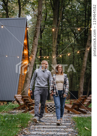 Romantic walk through nature near a cozy wooden cabin, capturing the charm of outdoor getaways Romantic walk through nature near a cozy wooden cabin, capturing the charm of outdoor getaways 119464582