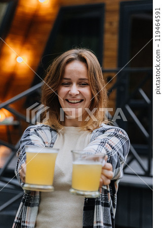 Woman offering two glasses of beer, smiling, inviting for toast, autumn gatherings outdoors 119464591