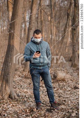 Man in a Forest Checking His Phone While Wearing a Mask Man in a Forest Checking His Phone While Wearing a Mask 119464760