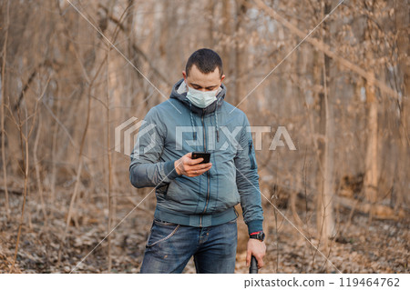 Man in a Mask Checking Phone in a Bare Forest Man in a Mask Checking Phone in a Bare Forest 119464762