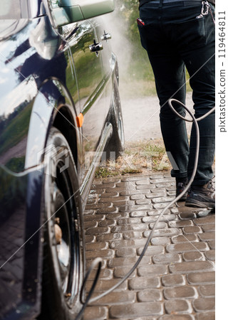Person Using a Pressure Washer to Clean a Dark Blue Car on a Cobblestone Driveway Person Using a Pressure Washer to Clean a Dark Blue Car on a Cobblestone Driveway 119464811