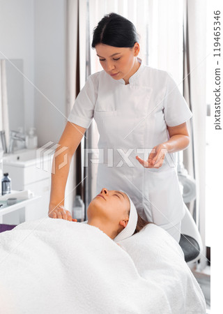 Cosmetologist woman massaging female client's Cosmetologist woman massaging female client's 119465346