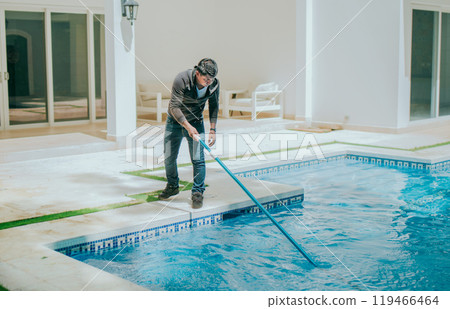 Man cleaning swimming pool with a suction hose. Worker cleaning a home pool with a vacuum hose 119466464
