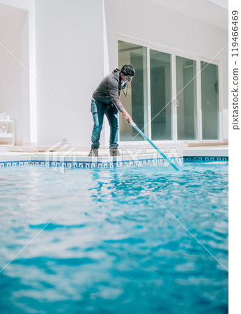 Young man cleaning a swimming pool with suction hose. Swimming pool cleaning and maintenance service 119466469