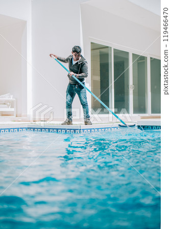 Home pool cleaning with wall brush. Male worker cleaning a home swimming pool with special brush 119466470