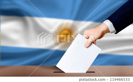 Argentina electoral elections concept. Hand holding ballot in voting ballot box with Argentina flag in background. Hand man puts ballot paper in voting box on Argentina flag background 119466533