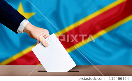 Hand holding ballot in voting ballot box with Democratic Republic of the Congo flag in background. Presidential elections of the democratic republic of the congo Hand holding ballot in voting ballot box with Democratic Republic of the Congo flag in background. Presidential elections of the democratic republic of the congo 119466534