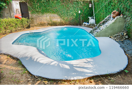 Crystal water home pool surrounded by a garden. Swimming pool designs for the home. Home swimming pool maintenance concept. Homemade swimming pool in a garden Crystal water home pool surrounded by a garden. Swimming pool designs for the home. Home swimming pool maintenance concept. Homemade swimming pool in a garden 119466660