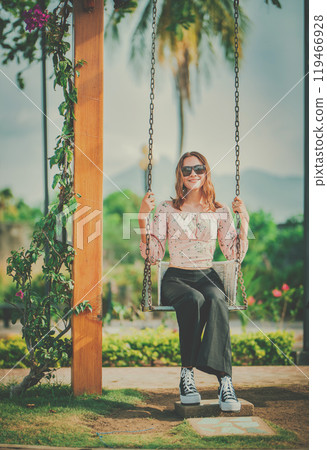 Portrait of a smiling girl sitting on a swing in a nature park. Happy young woman sitting on a swing in a nature park 119466928