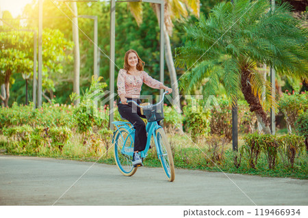 Cheerful Latin girl riding a bicycle in a green park. Beautiful and smiling young woman riding a bicycle in a nice park, looking at camera 119466934