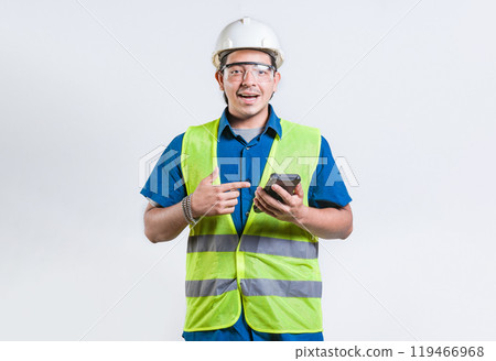 Smiling engineer holding phone and looking at camera isolated. Latin male builder engineer using phone isolated 119466968