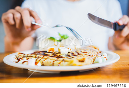 Close up of woman eating a chocolate crepe with fork. Woman hands eating chocolate crepe and ice cream with fork 119467338