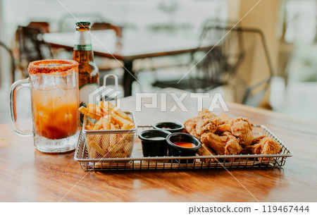 Delicious spicy chicken wings with fries and michelada accompanied by beer served on a restaurant table Delicious spicy chicken wings with fries and michelada accompanied by beer served on a restaurant table 119467444