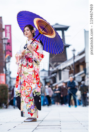 A young woman in a long-sleeved kimono posing in front of the Toki no Kane bell 119467469