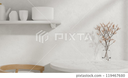 A round white dining table with a vase, a wooden armchair, and a wall shelf displaying kitchenware. A round white dining table with a vase, a wooden armchair, and a wall shelf displaying kitchenware. 119467680
