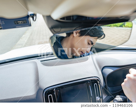 The facial expression of a male driver asleep while driving through the rearview mirror 119468106